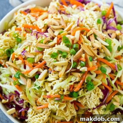 A bowl of ramen noodle salad with cabbage, noodles, green onions and almonds.