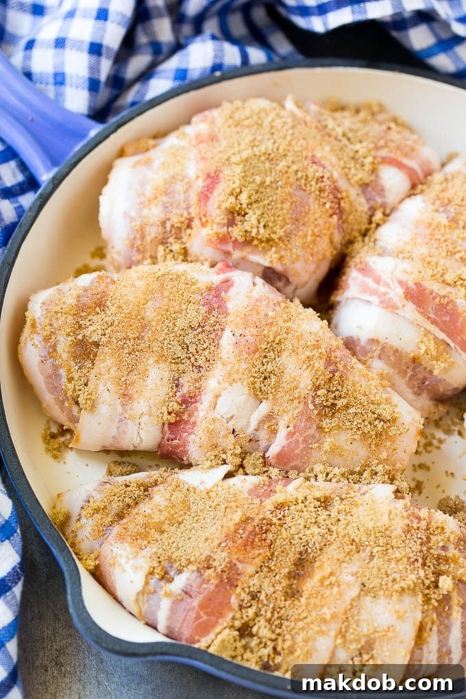 Seasoned chicken breasts neatly wrapped in strips of thin-cut bacon, positioned in a baking pan, ready for the oven.
