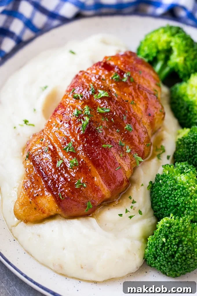Plated bacon wrapped chicken, artfully served over a bed of creamy mashed potatoes with vibrant green steamed broccoli on the side.