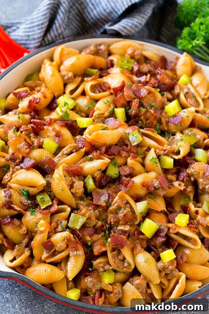 Cheeseburger pasta in a skillet topped with pickles and bacon.