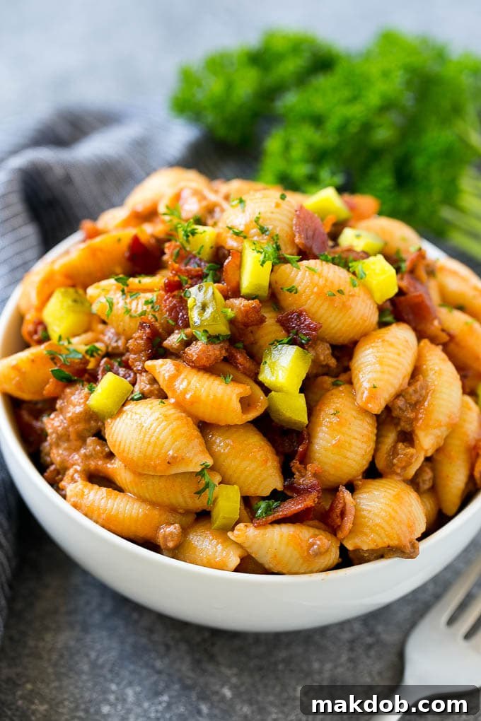 A bowl of cheeseburger pasta topped with bacon and chopped pickles.