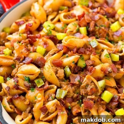 A pan of pasta with ground beef, onion, pasta shells, cheddar cheese and bacon.