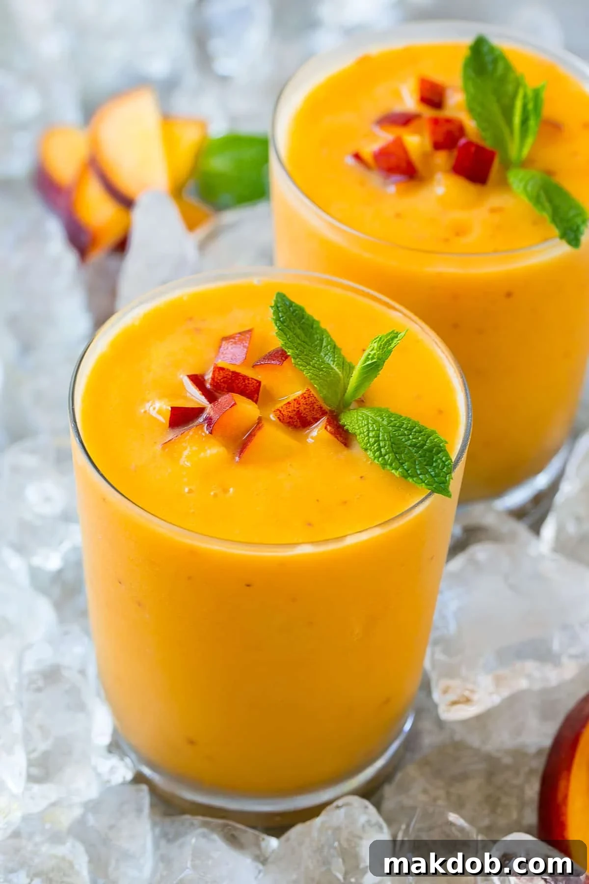 A glass of peach smoothie topped with chopped peaches and fresh mint.