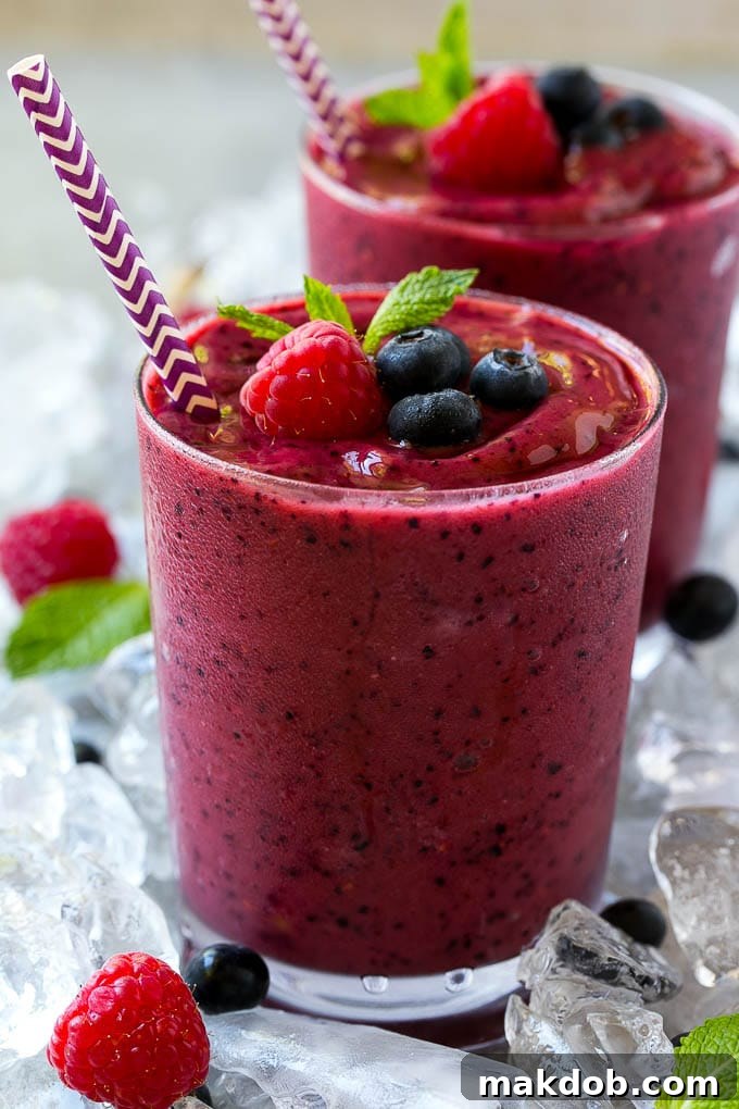 A glass of frozen fruit smoothie with a straw, topped with raspberries, blueberries and mint.