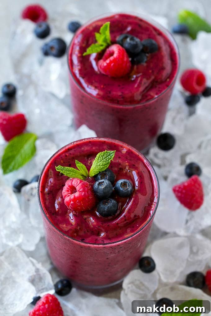 Frozen fruit smoothies on a bed of ice with blueberries and raspberries.
