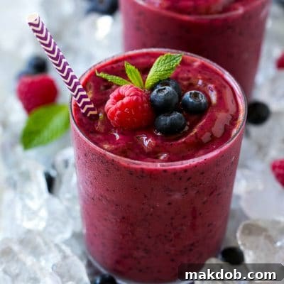 A glass of frozen fruit smoothie in crushed ice, garnished with berries and mint.