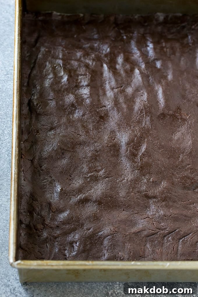 Chocolate cake crust pressed into a baking pan for a chocolate gooey butter cake.
