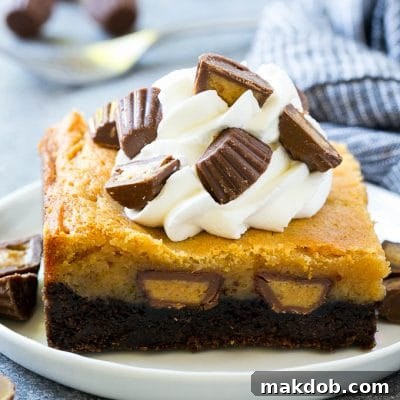 Peanut butter chocolate gooey butter cake topped with whipped cream and chopped peanut butter cups.