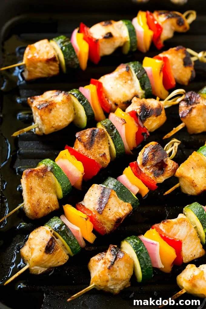Perfectly cooked grilled chicken and vegetable kabobs resting on a grill pan, ready to be served, garnished with fresh herbs.