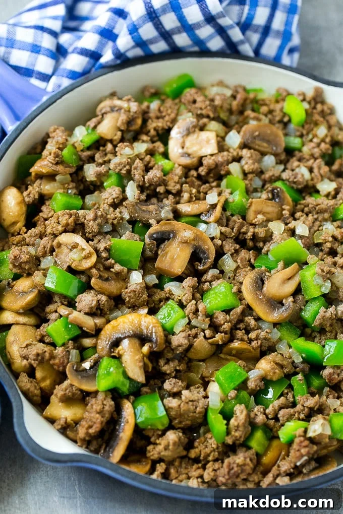A skillet of browned hamburger meat, mushrooms, onions and bell peppers.