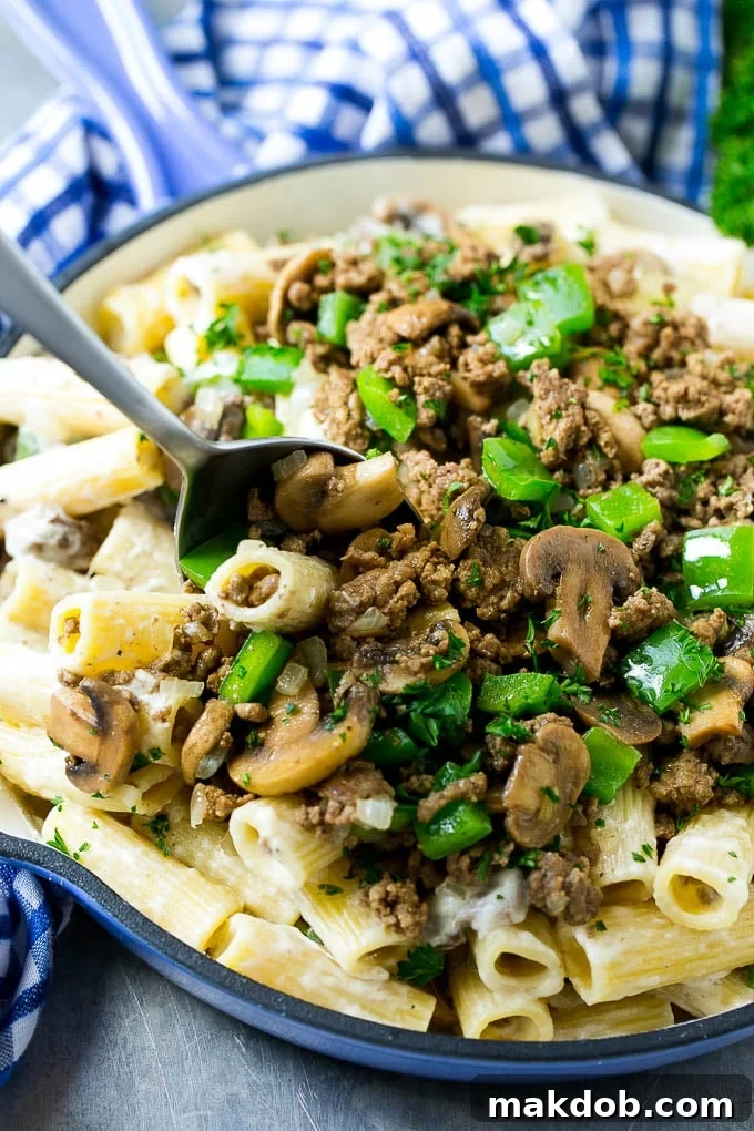 A pan of philly cheesesteak pasta with a serving spoon in it.