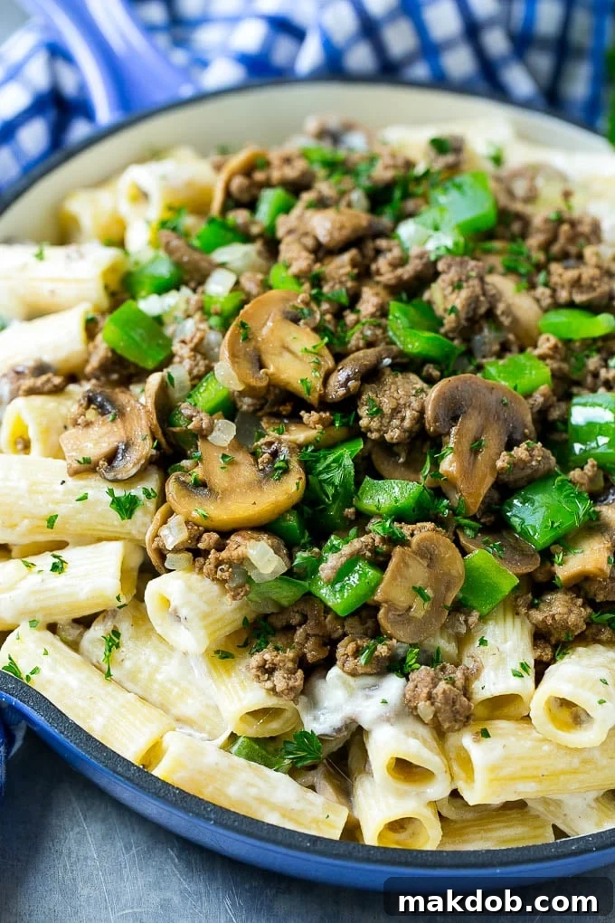 A skillet of philly cheesesteak pasta with creamy rigatoni, ground beef, sauteed mushrooms and green peppers.