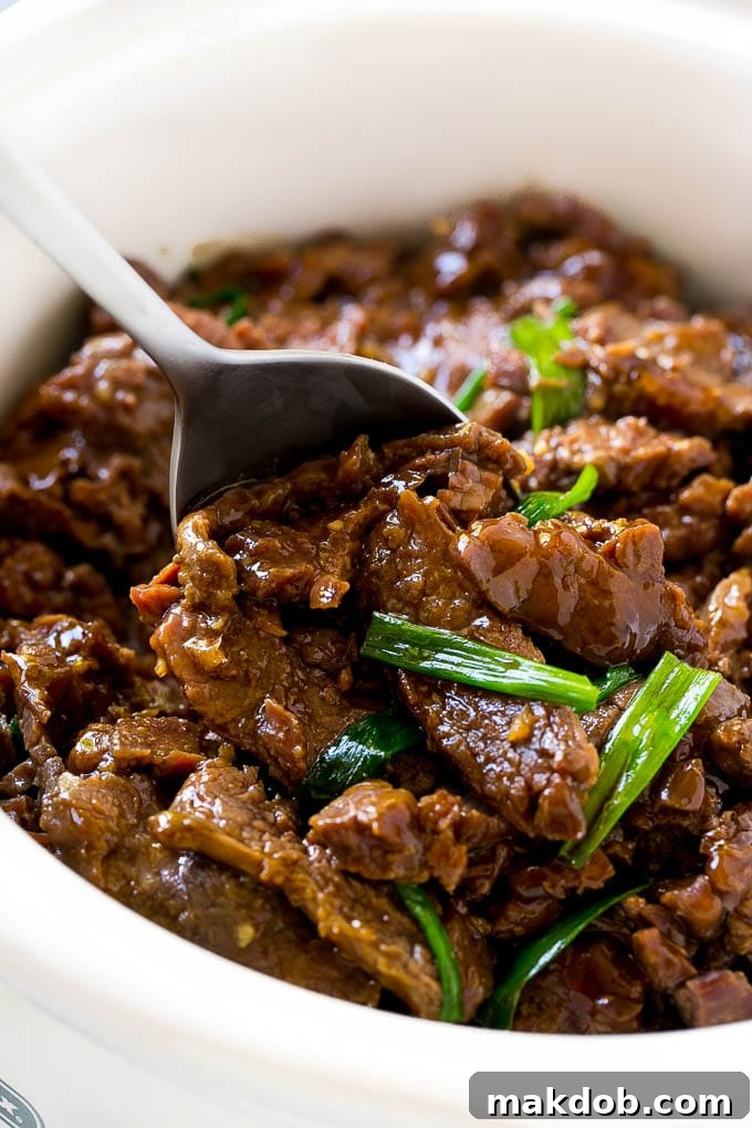 A slow cooker full of Mongolian beef in a savory sauce with green onions.