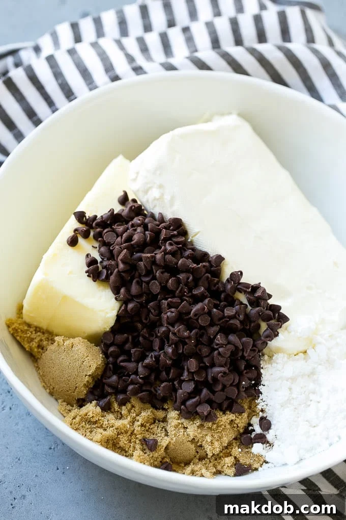 A curated selection of essential ingredients including softened butter, rich cream cheese, sweet brown sugar, and vibrant chocolate chips, all prepped for making the delicious cookie dough dip.