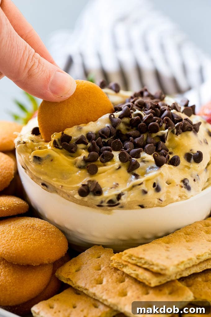 A crisp cookie poised to scoop into a generous bowl of delectable edible cookie dough dip, showcasing its creamy texture and inviting appearance.