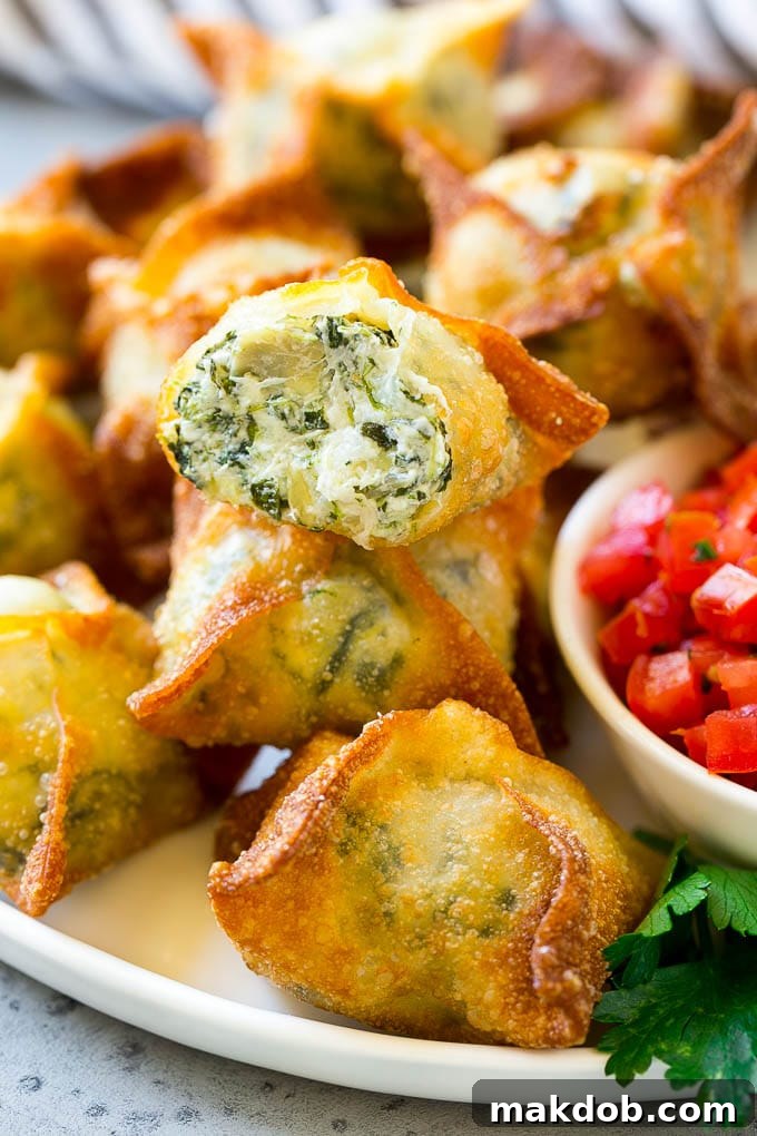 Spinach artichoke wontons with homemade spinach artichoke dip stuffed into wonton wrappers and fried, served on a white plate with fresh herbs.