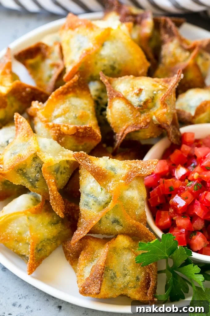 A serving plate piled high with golden-brown spinach artichoke wontons, garnished with fresh herbs.