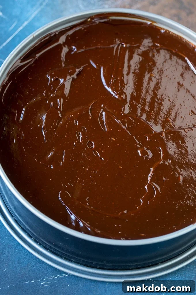 Ultimate No-Bake Oreo Cheesecake 5 A thick, glossy layer of chocolate ganache being poured and spread evenly over the top of a no bake Oreo cheesecake.
