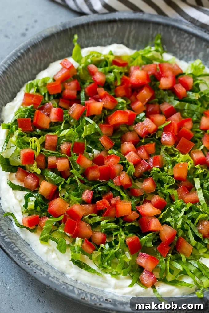 The Ultimate BLT Dip 5 A close-up of the BLT dip, showcasing fresh lettuce and ripe tomatoes on top of the creamy ranch base, before the final bacon and green onion layers.