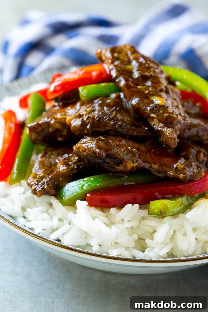 A bowl of rice topped with pepper steak stir fry.