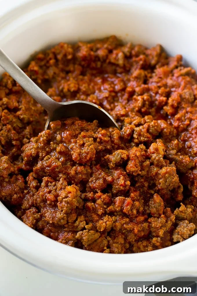 Slow Cooker Sloppy Joes Recipe | Crock Pot Sloppy Joes | Homemade Sloppy Joes #beef #slowcooker #crockpot #sandwich #dinneratthezoo Slow cooker sloppy joe meat with a serving spoon.