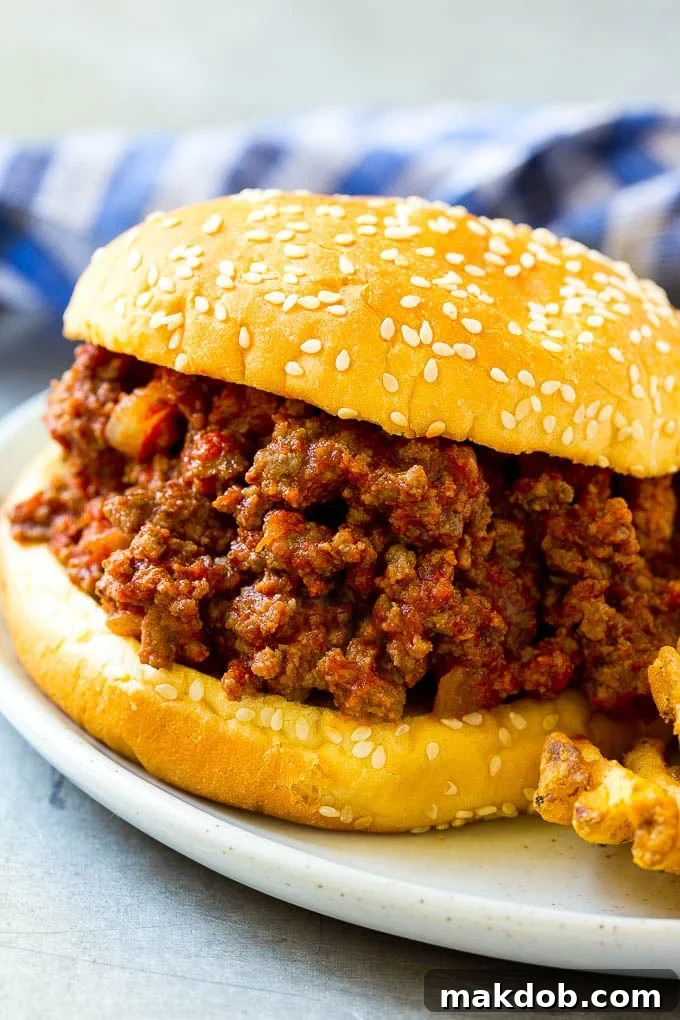 Slow Cooker Sloppy Joes Recipe | Crock Pot Sloppy Joes | Homemade Sloppy Joes #beef #slowcooker #crockpot #sandwich #dinneratthezoo A crock pot sloppy joe on a hamburger bun served with french fries.