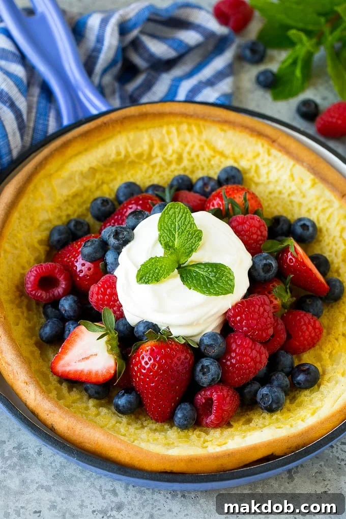 A Dutch baby puffed pancake in a skillet, topped with berries and whipped cream.