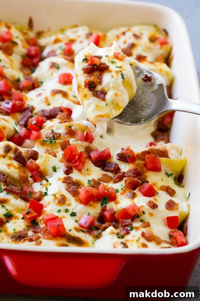 A pan of chicken alfredo stuffed shells with a serving spoon.