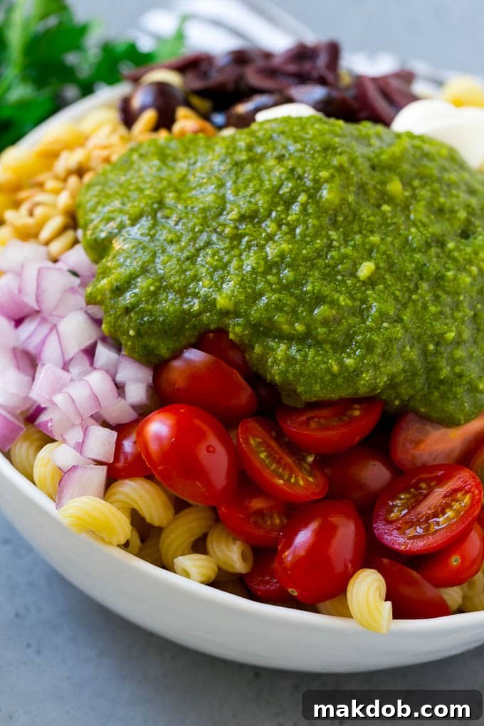 A close-up shot showing colorful vegetables and corkscrew pasta generously coated with fresh green pesto, ready to be tossed.