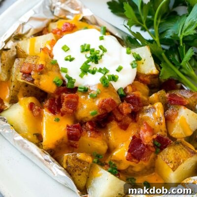 Grill-Wrapped Potatoes 7 Grilled potatoes in foil on a serving plate garnished with herbs.