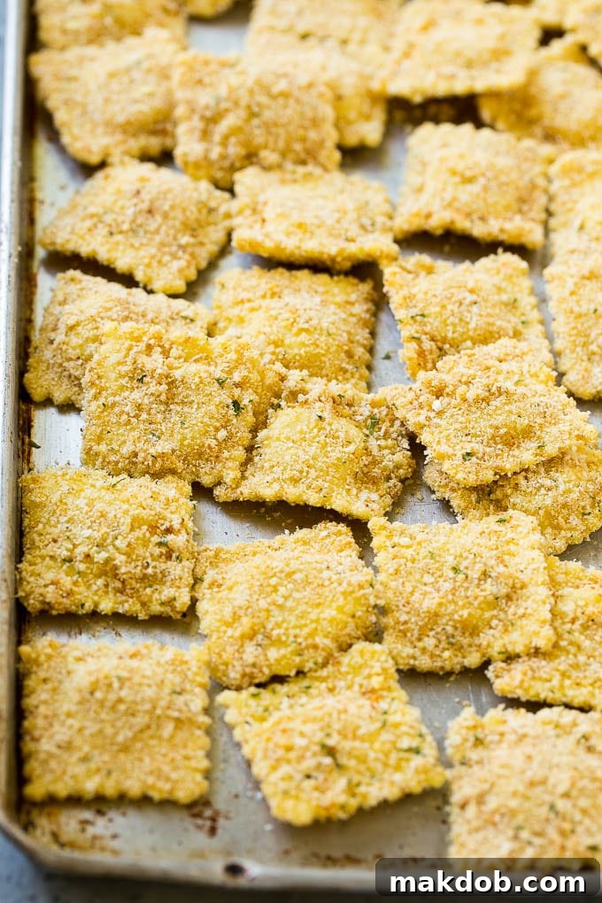 Breaded ravioli on a sheet pan ready to be fried.