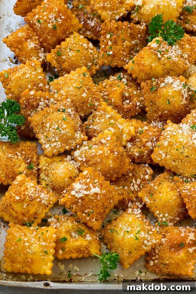 A pile of fried ravioli topped with parmesan cheese and chopped parsley.