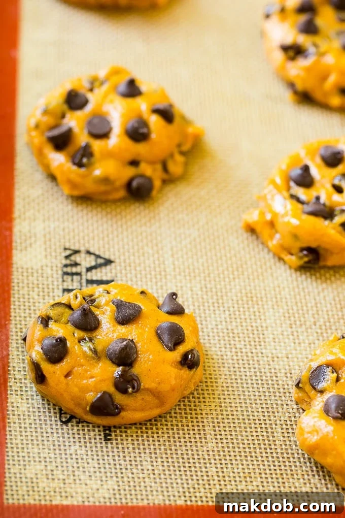 Cookie dough ready for baking Portioned pumpkin chocolate chip cookie dough on a baking sheet lined with parchment paper, ready for baking.