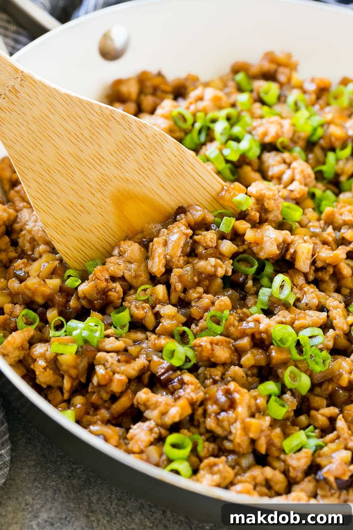 Close-up of savory ground chicken mixture in a pan, infused with sauce and topped with fresh green onions, ready for serving.