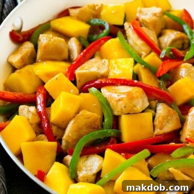 Mango chicken in a skillet with red and green sliced peppers.