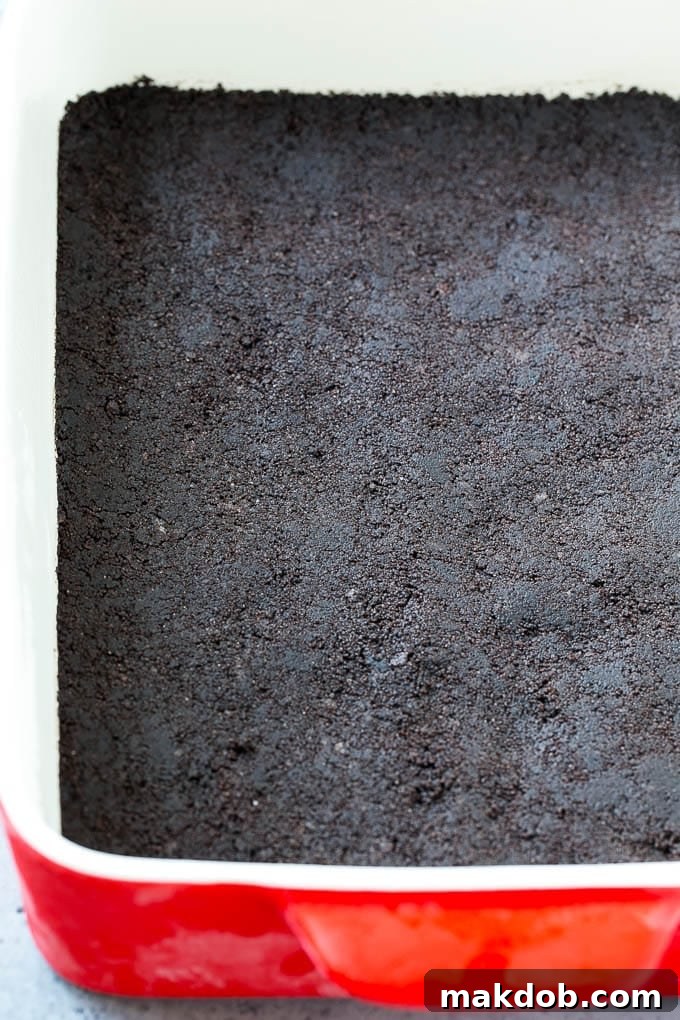 A pristine, dark Oreo cookie crust, evenly pressed into the bottom of a rectangular glass baking dish, forming the perfect base for a no-bake chocolate lasagna.
