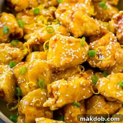 Chinese lemon chicken in a frying pan, garnished with lemon zest, sesame seeds and green onions.