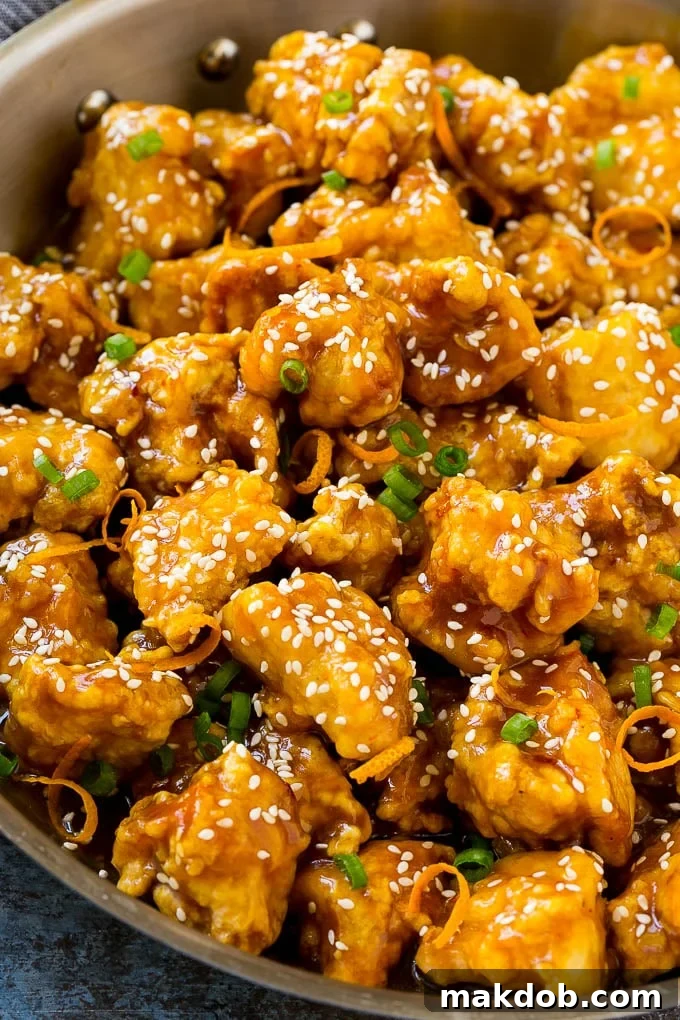 Orange chicken in a skillet with crispy chicken, sesame seeds, orange zest and green onions.
