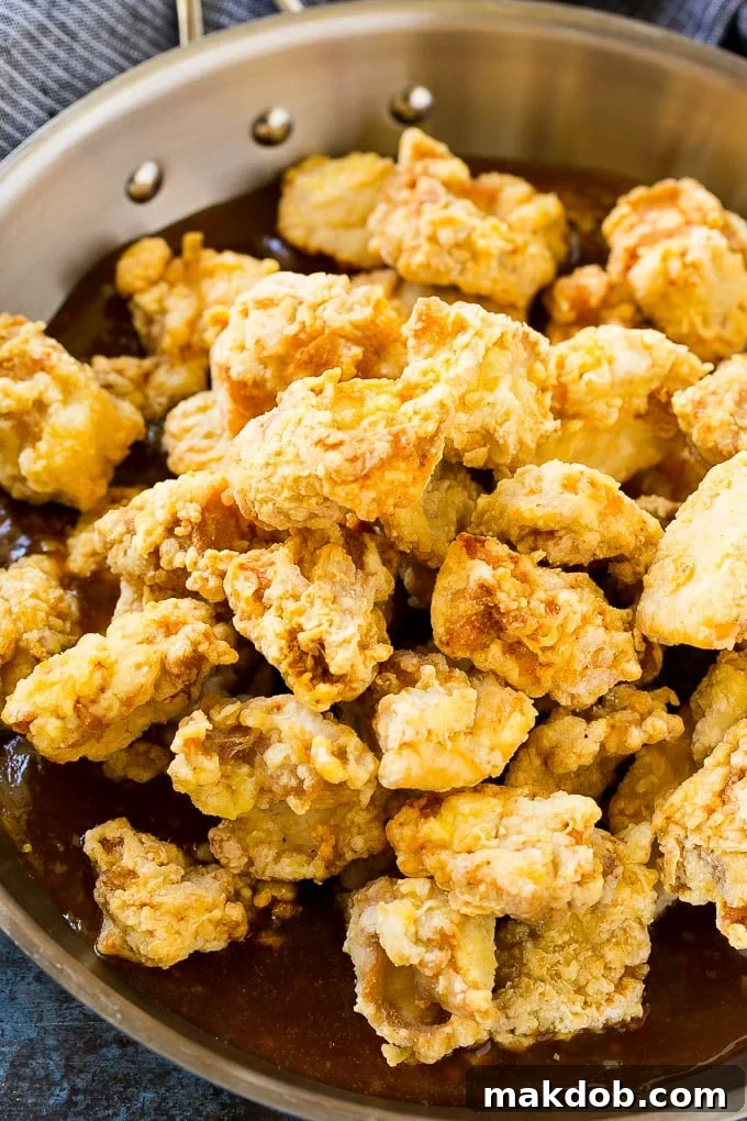 Crispy chicken pieces in a pan of orange sauce.