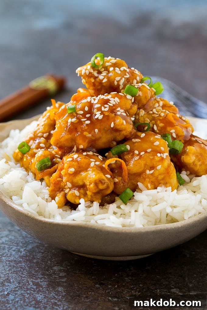 A bowl of orange chicken served over steamed rice and topped with sesame seeds.