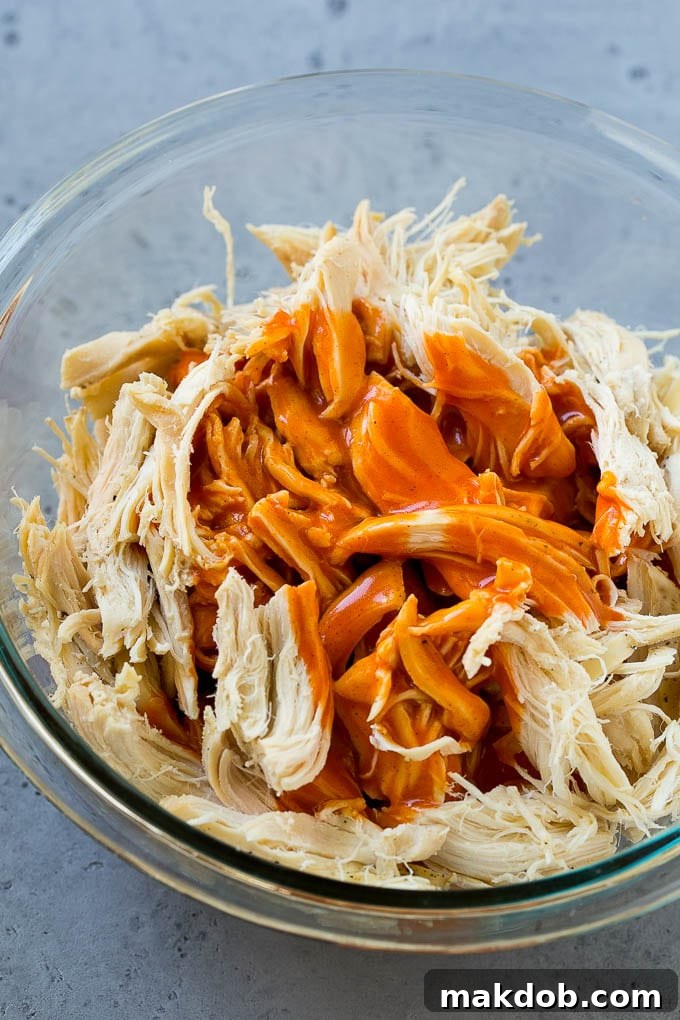 A close-up of shredded chicken drenched in vibrant buffalo sauce, ready to be layered into delicious sliders.