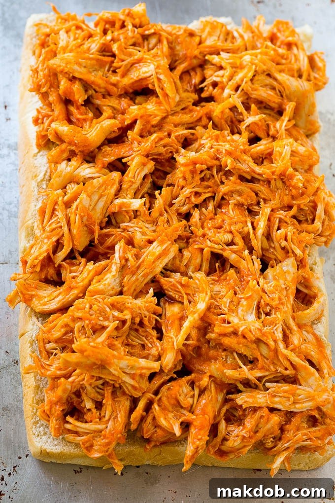 Shredded buffalo chicken spread evenly over the toasted bottom halves of slider buns, forming the core of the sandwich.