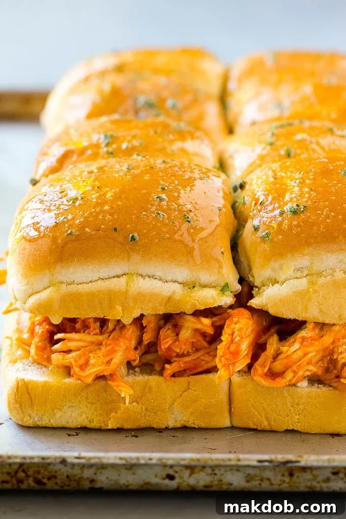 Buffalo chicken sliders assembled with chicken and buns, brushed with garlic butter, ready for baking.