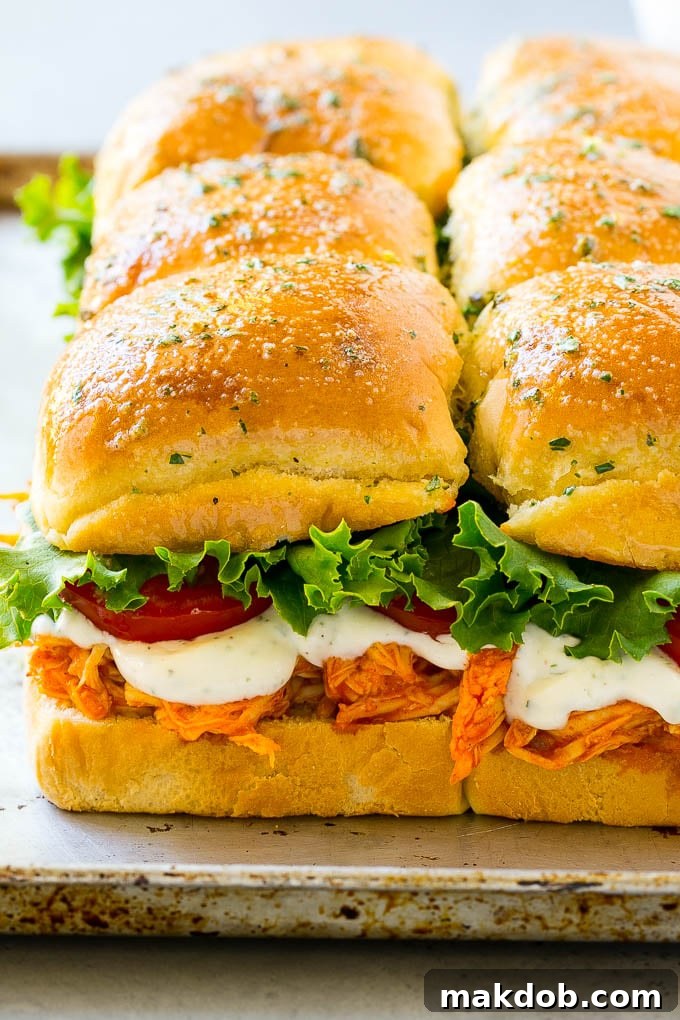 A tantalizing spread of Buffalo Chicken Sliders, featuring the vibrant colors of shredded buffalo chicken, crisp lettuce, ripe tomato, and a generous drizzle of creamy ranch sauce, all nestled in soft, toasted slider buns.