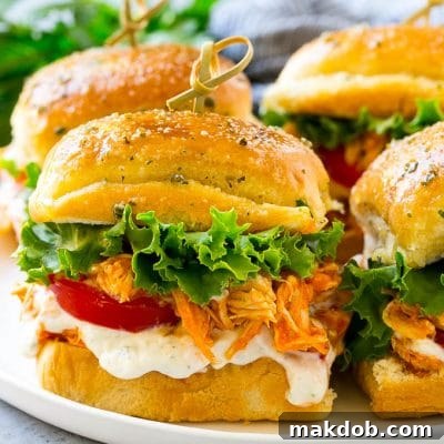A plate of buffalo chicken sliders layered with lettuce, tomato and ranch.