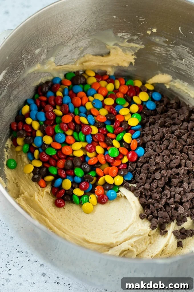 Cookie dough in a mixing bowl with chocolate chips and M&M's.