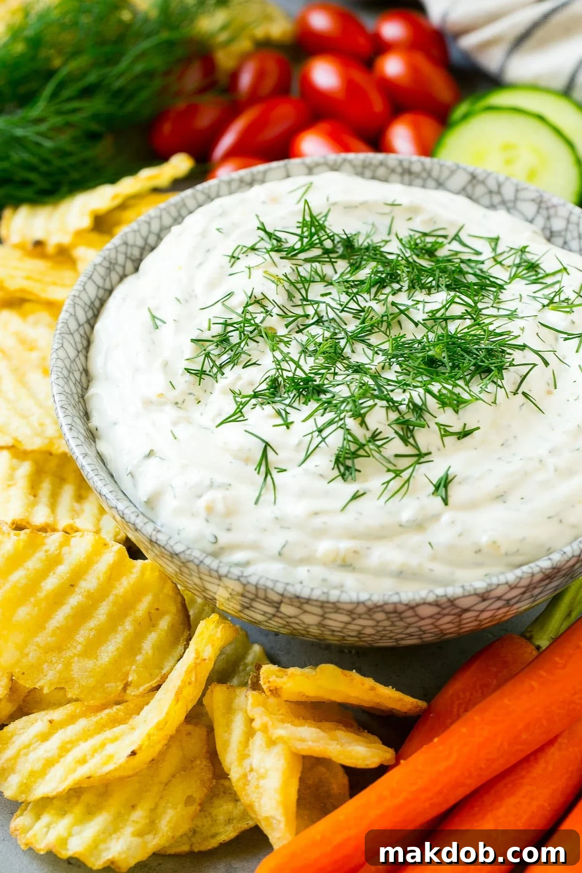 Creamy Dill Delight 6 A side view of a bowl of dill dip served with potato chips, carrots and cucumbers.
