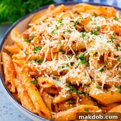 A bowl of penne alla vodka pasta topped with parmesan cheese, parsley and red pepper flakes.