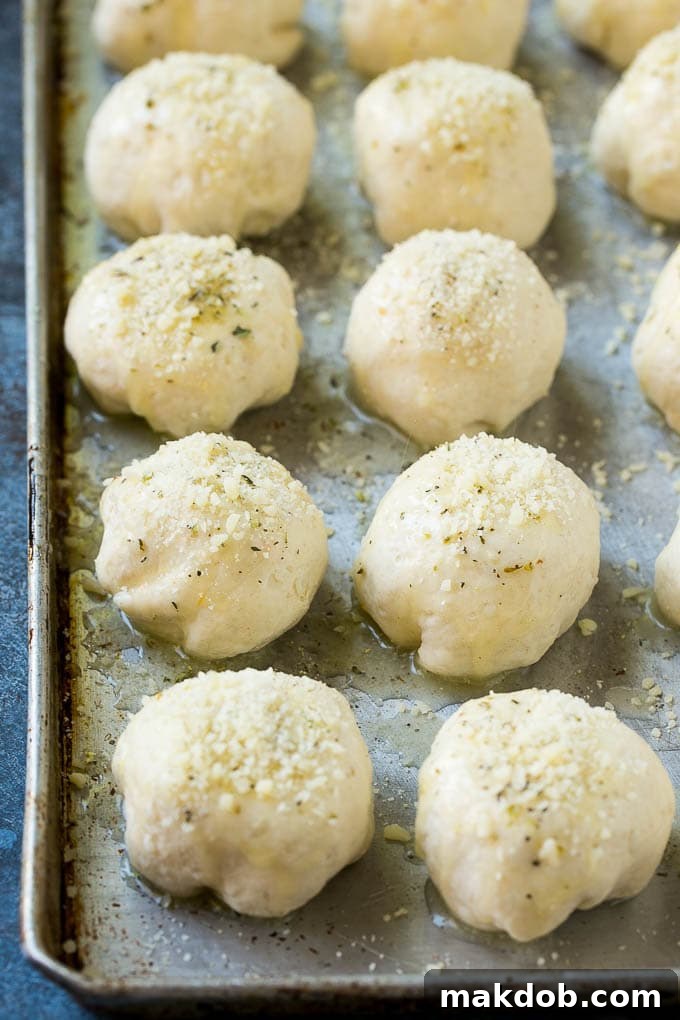 Unbaked cheese bombs neatly arranged on a baking sheet, brushed with melted garlic butter and generously sprinkled with grated Parmesan cheese.