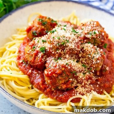 Slow cooker meatballs served over spaghetti, topped with parsley and parmesan cheese.